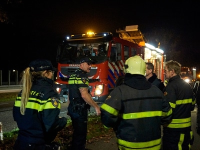 Brandweerlieden en agenten staan in het donker bij een brandweerauto