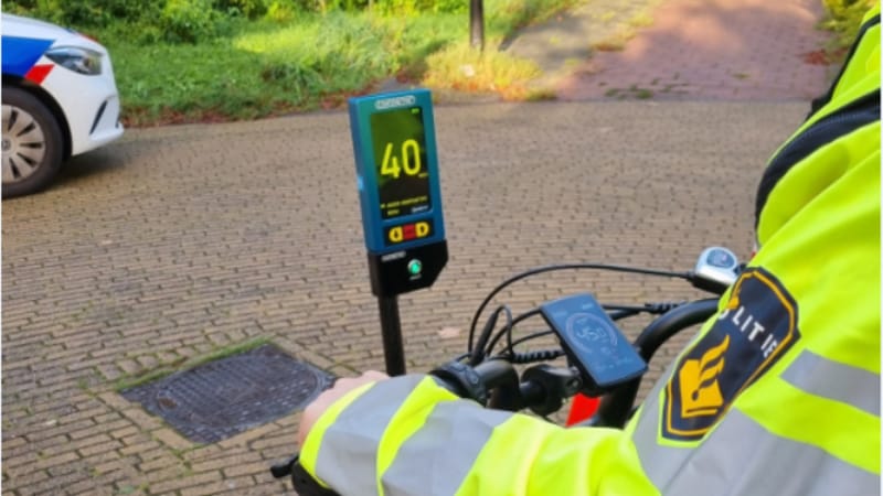 je ziet een agent die de snelheid van een elektrische fiets meet op een rollenbank